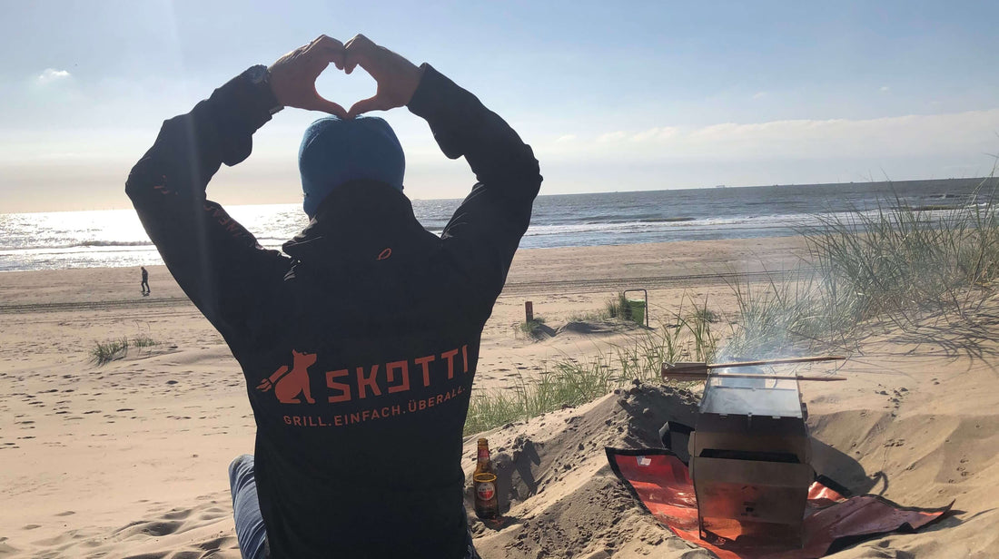 Mann grillt mit kompakten SKOTTI Grill am Strand 